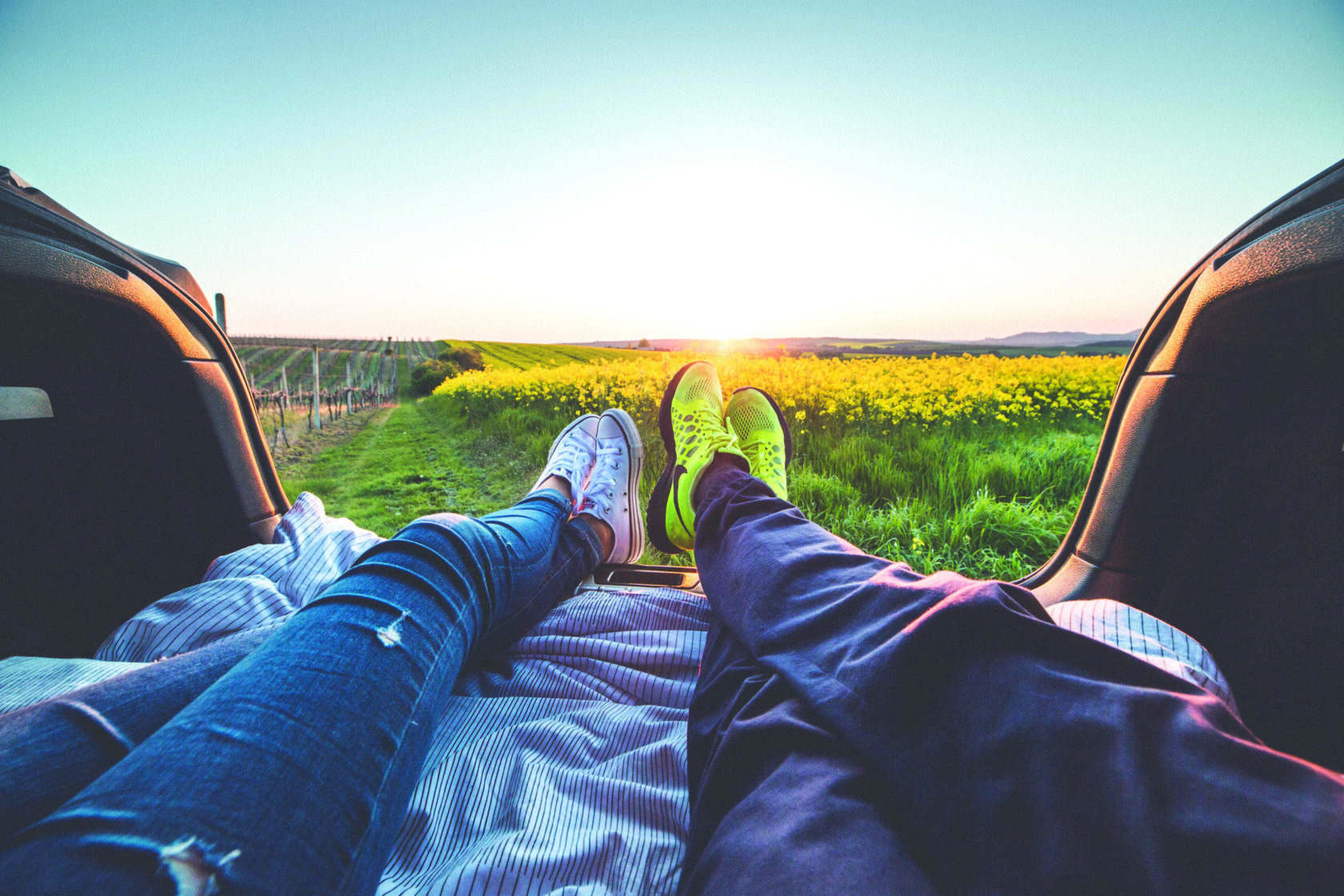 Two people laying down in the trunk of a car looking out at a field of flowers.